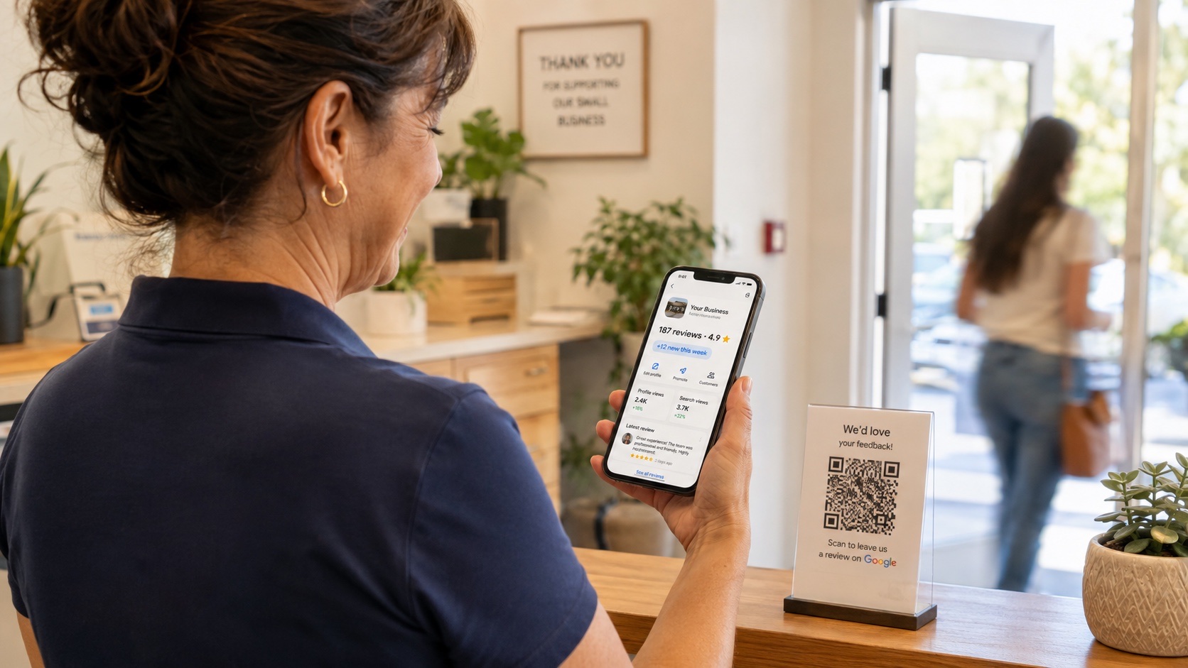 Small business owner smiling at her phone showing a Google Business Profile with 187 reviews and a 4.9 star rating, with a QR code on the counter beside her